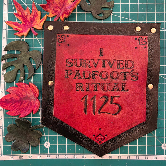 Orange and black leather tag with text on a cutting mat with leaves
